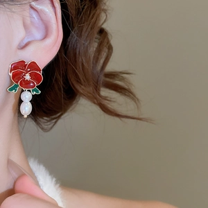 Detail of red floral earrings with white pearls on a model, featuring vintage style