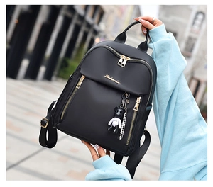 Detail of black nylon backpack featuring gold zippers and a cute bear keychain accessory