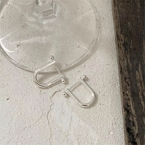 Macro shot of minimalist silver U-shaped horseshoe stud earrings on textured stone surface