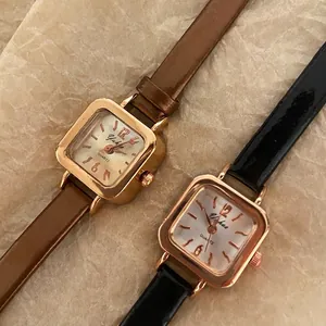 Minimalist square rose gold watches with brown and black leather straps on marble