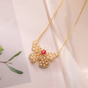 Close-up of golden butterfly pendant with white pearls, red gemstone and zircons