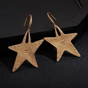 Detailed view of gold-tone star earrings with retro hammered texture on dark background