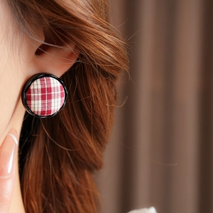 Close-up of model wearing round red and white plaid fabric earrings with black borders
