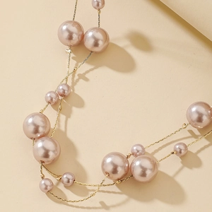 Macro detail of multi-layered pink faux pearl necklace with gold chain elements