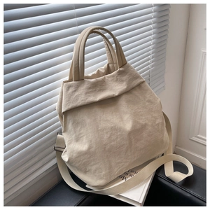 Detail of beige nylon tote bag with pleated texture and adjustable strap on a sofa