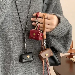 Three leather mini pouch necklaces in burgundy, black and brown on a grey sweater
