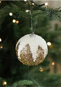 Gros plan d'une boule de Noël à paillettes dorées suspendue sur un sapin de Noël vert