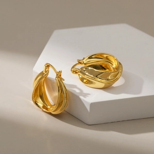 Chunky 18K gold plated hoop earrings with irregular twisted design on white pedestal