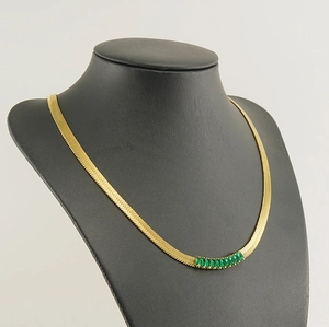 Detail of 18K gold plated snake chain necklace with green zircon stones on black mannequin