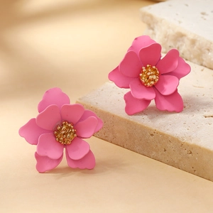 Close-up of pink layered petal earrings with golden stamens on a textured stone base
