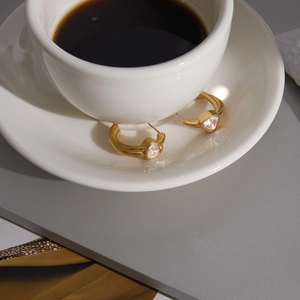 Close-up of gold C-shaped hoop earrings with heart-shaped zircon on a white cup rim