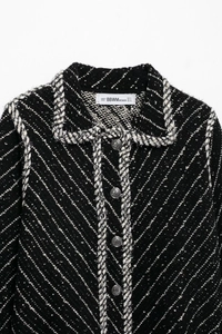 Close-up of black tweed jacket with silver buttons and woven trim details on collar