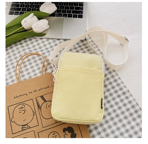 Detail view of a yellow canvas crossbody phone bag featuring a front pocket and white strap