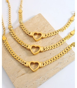 Close-up of three gold-plated Cuban chain bracelets with hollow heart charms on marble
