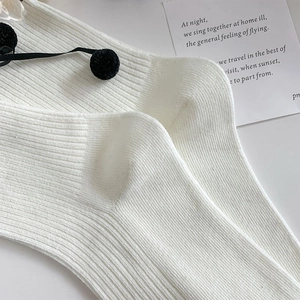 Detail of white ribbed knit socks featuring elegant black bow ties and fuzzy pom-poms