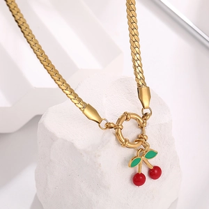 Close-up of a gold snake chain necklace with red cherry pendant on white stone