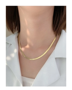 Close-up of polished gold flat snake bone choker necklace worn with a white shirt