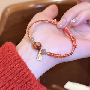 Detailansicht eines geflochtenen roten Armbands mit Achatperlen und Kürbis-Anhänger