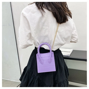 Detail of purple croc-textured mini bag with golden chain strap on a model