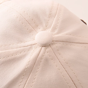 Close-up of the cream cotton baseball cap showing top button and quality stitching