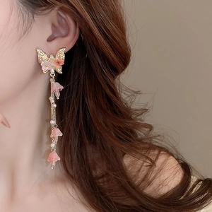 Détail de boucles d'oreilles papillon dorées avec pétales roses et perles sur un modèle