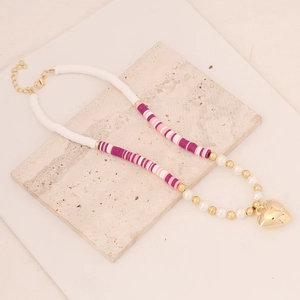 Bohemian clay bead necklace with pearls and gold heart pendant on a stone surface