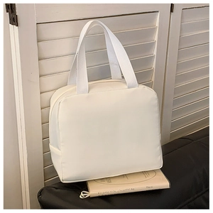 Close-up of a white insulated canvas lunch bag on a black leather sofa near a window