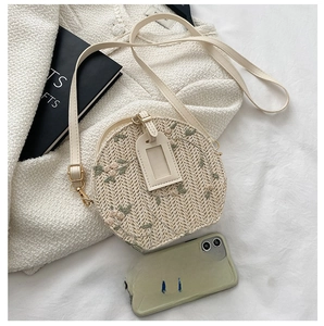 Detail shot of a round straw crossbody bag featuring delicate floral embroidery and leather strap