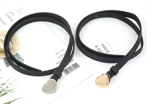 Detail of slim black PU leather belts featuring gold and silver heart-shaped metal buckles