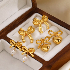 Set de boucles d'oreilles nœuds dorés 18K avec perles et cœurs sur velours blanc