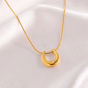 Macro view of gold-plated U-shaped pendant on a snake chain over white silk fabric