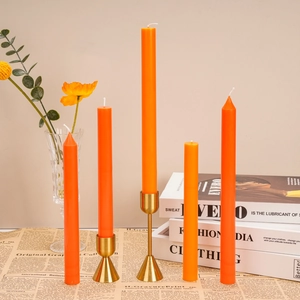 Artistic presentation of tall orange taper candles on golden holders with vintage paper decor