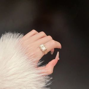 Detail of a gold watch-style ring with shimmering crystals and a pearlescent center