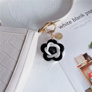 Detail of faux leather camellia flower keychain with gold coin pendant on ivory bag