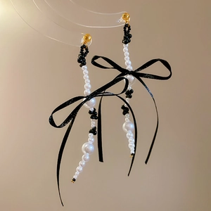 Detail of long pearl tassel earrings with black ribbon bows and golden accents