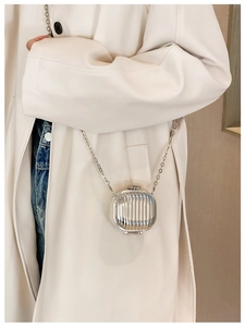 Close-up of a mini silver metal chain bag with vertical stripes worn on a beige trench coat