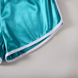 Detail of high-gloss teal athletic shorts with white edging and smooth silk-like texture