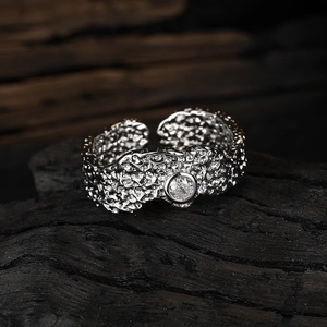 Irregular texture open ring in silver with a round clear gemstone on dark wood