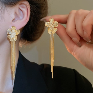 Detailed close-up of 18k gold flower earrings with pearls and long tassel snakeskin chains