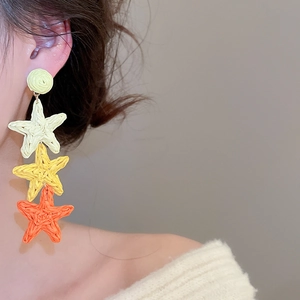 Detailed view of handmade raffia star tassel earrings in yellow and orange tones