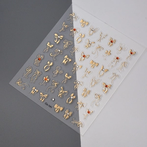 Detail showing 3D gold bow nail art stickers with red rhinestones on transparent sheet
