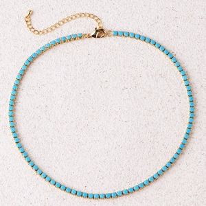 Detailed flat lay of gold tennis necklace with small turquoise stones and lobster clasp