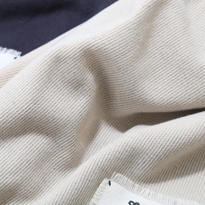 Close-up of beige twill knit fabric texture with soft folds and white woven label