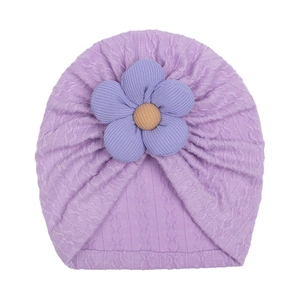 Detailed view of purple knit baby turban hat with a large floral decoration and soft texture