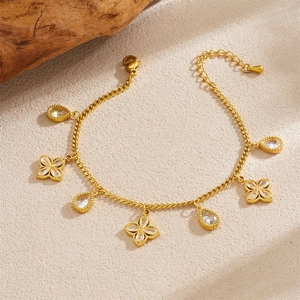 Gold plated bracelet with sparkling teardrop and floral crystal charms on stone background