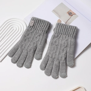 Détail de gants en maille torsadée grise avec étiquette en cuir marron au poignet