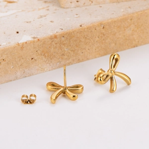 Elegant gold bow-shaped stainless steel earrings on a beige stone minimalist background
