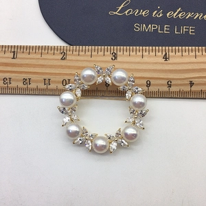 Detail of round golden brooch featuring white freshwater pearls and sparkling crystals