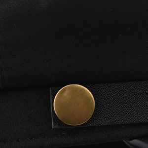 Close-up of golden metal button and black lychee texture leather strap on newsboy cap