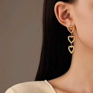 Minimalist triple heart drop earrings in gold finish worn by a model in lifestyle shot